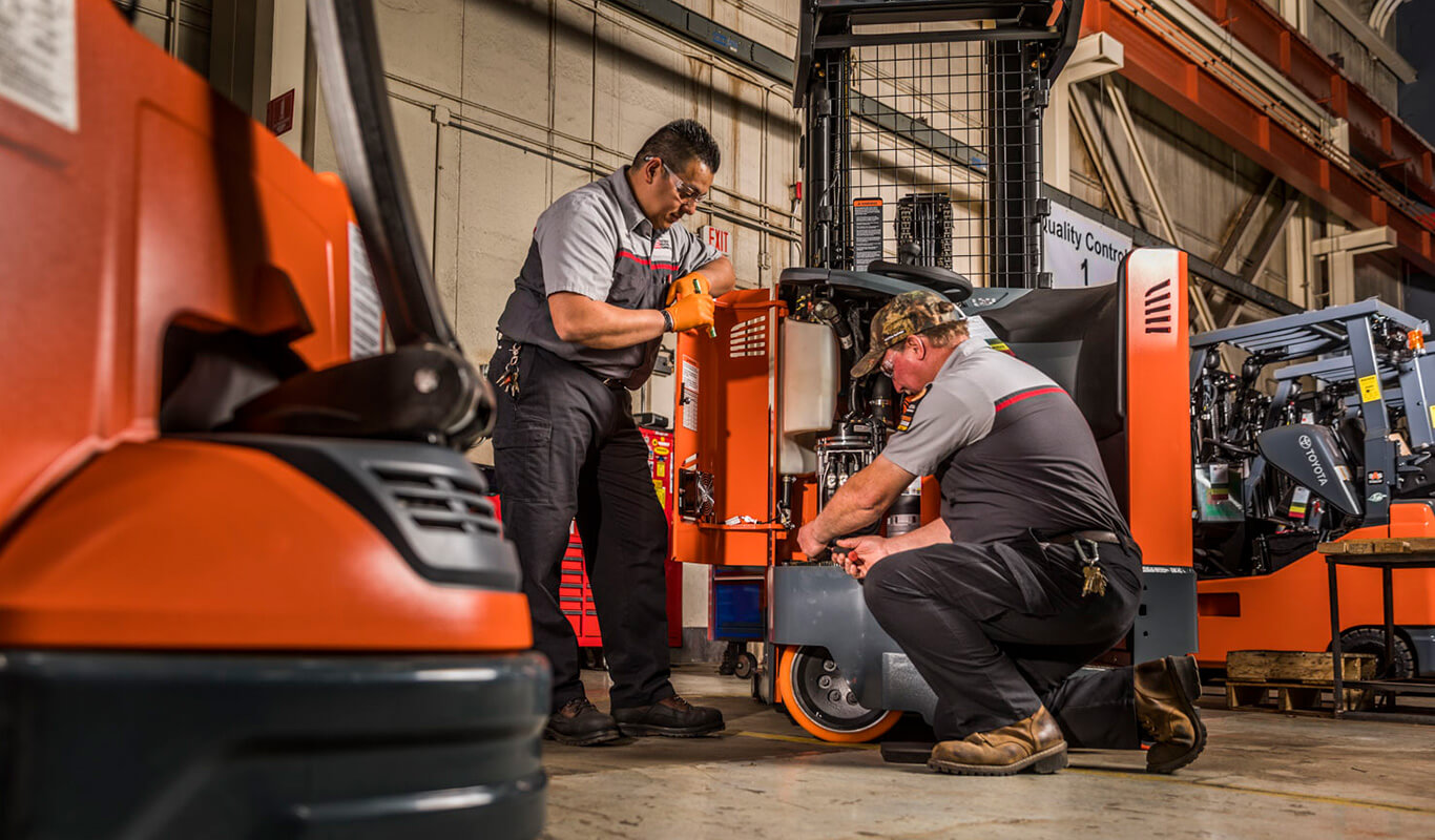 A technician oversees another equipment technician service a forklift