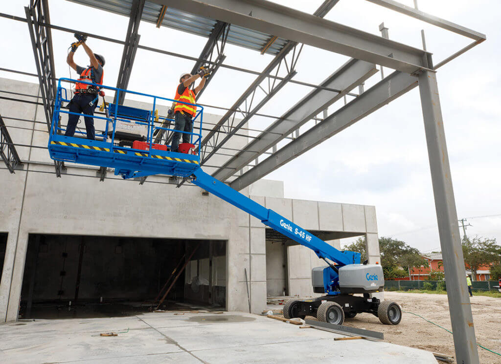Two construction workers use a boom lift to work on the frame of a ceiling of an industrial-looking building