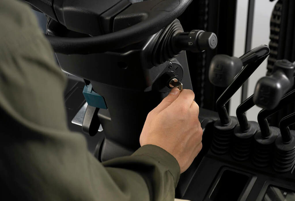 A close up of a person's hand turning the key to start the ignition of a forklift