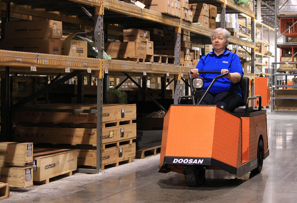 A woman drives a cart through a warehouse as she collects packages to ship